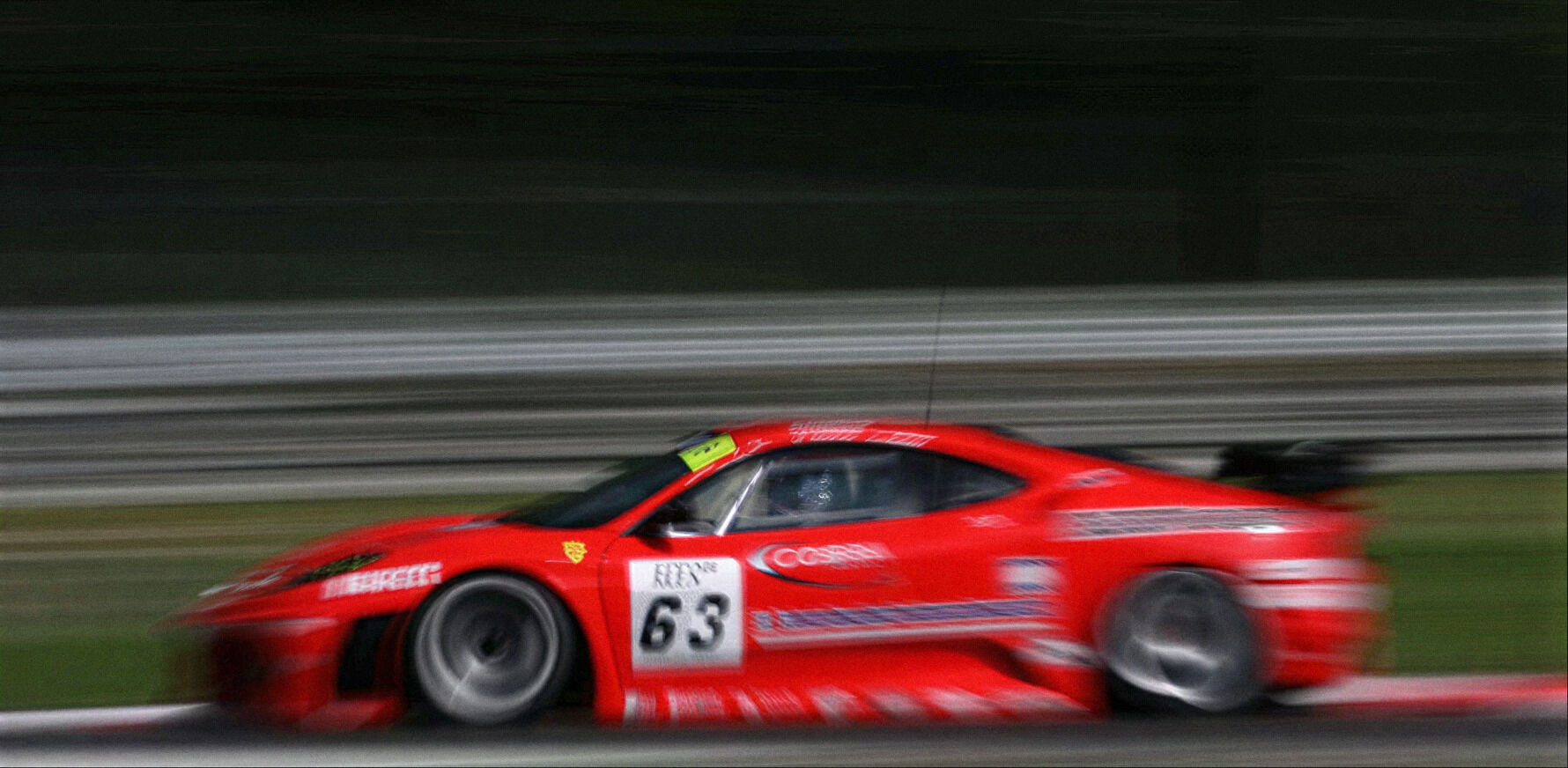 Red Ferrari racing car, number 63, at speed on track